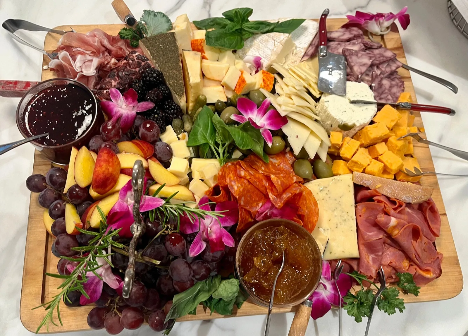 Overhead charcuterie board with cheeses, cured meats, grapes, orchids, and preserves
