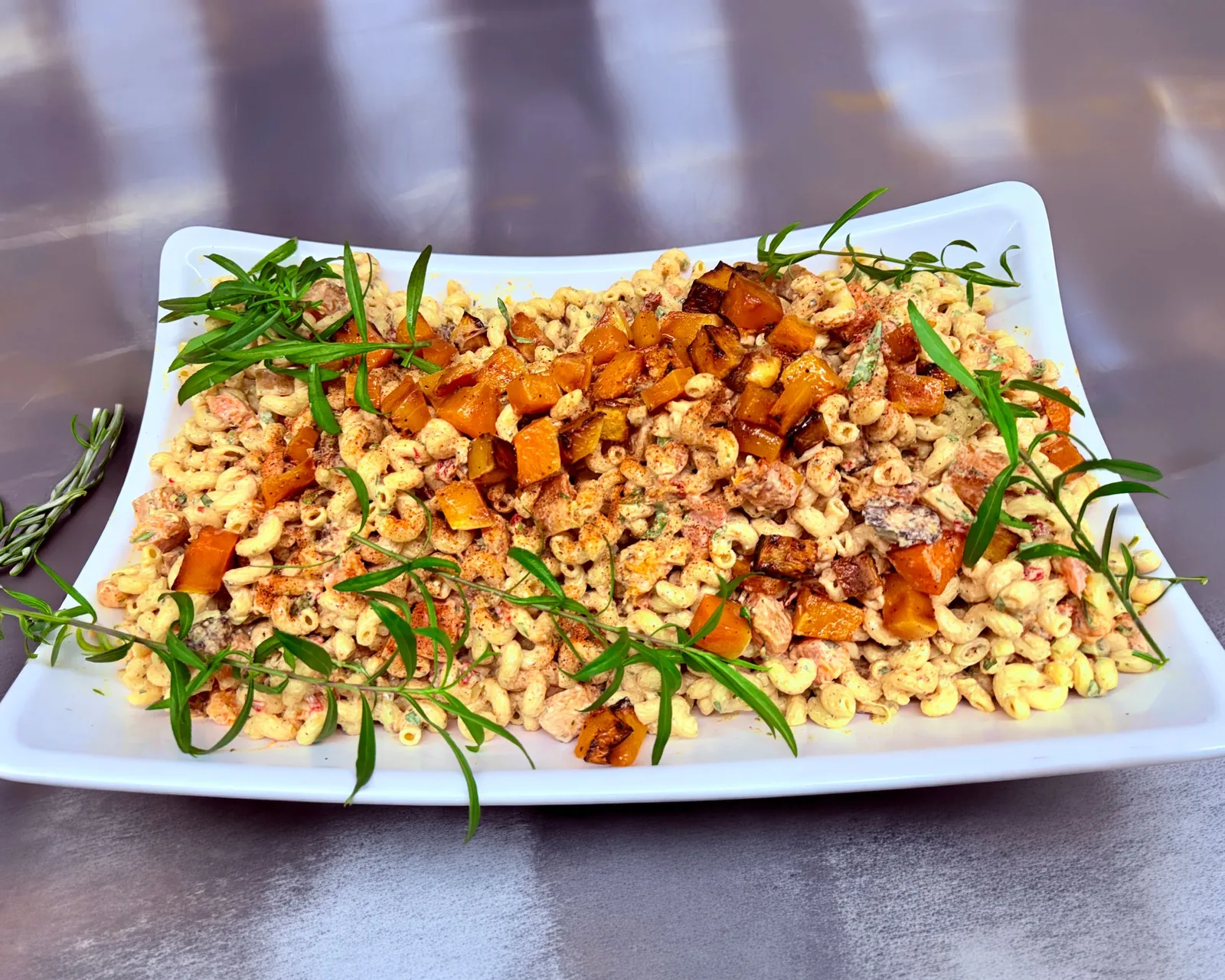 Macaroni salad with roasted peppers and fresh tarragon on a white platter