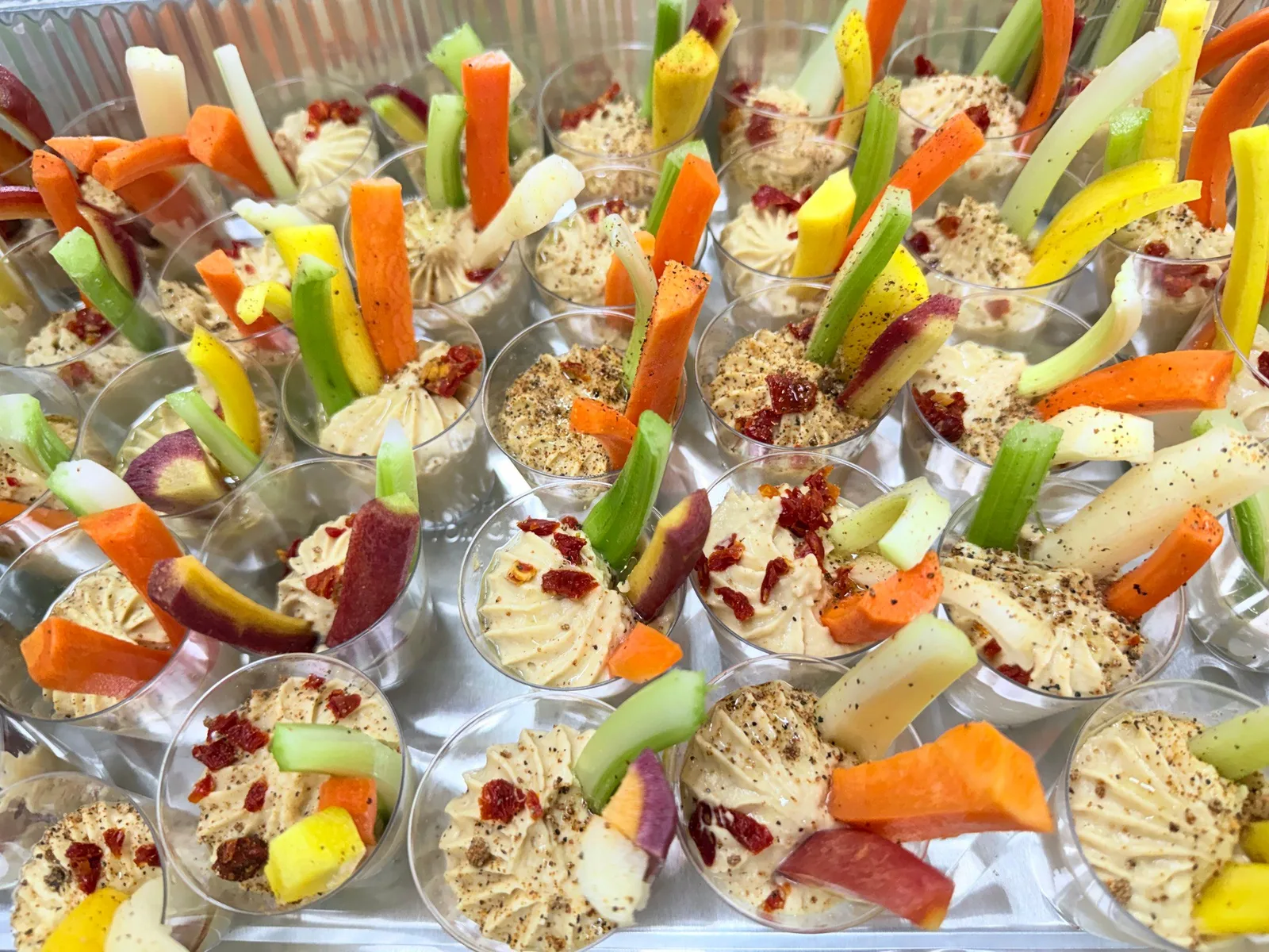 Individual hummus cups with colorful vegetable crudités and sun-dried tomatoes