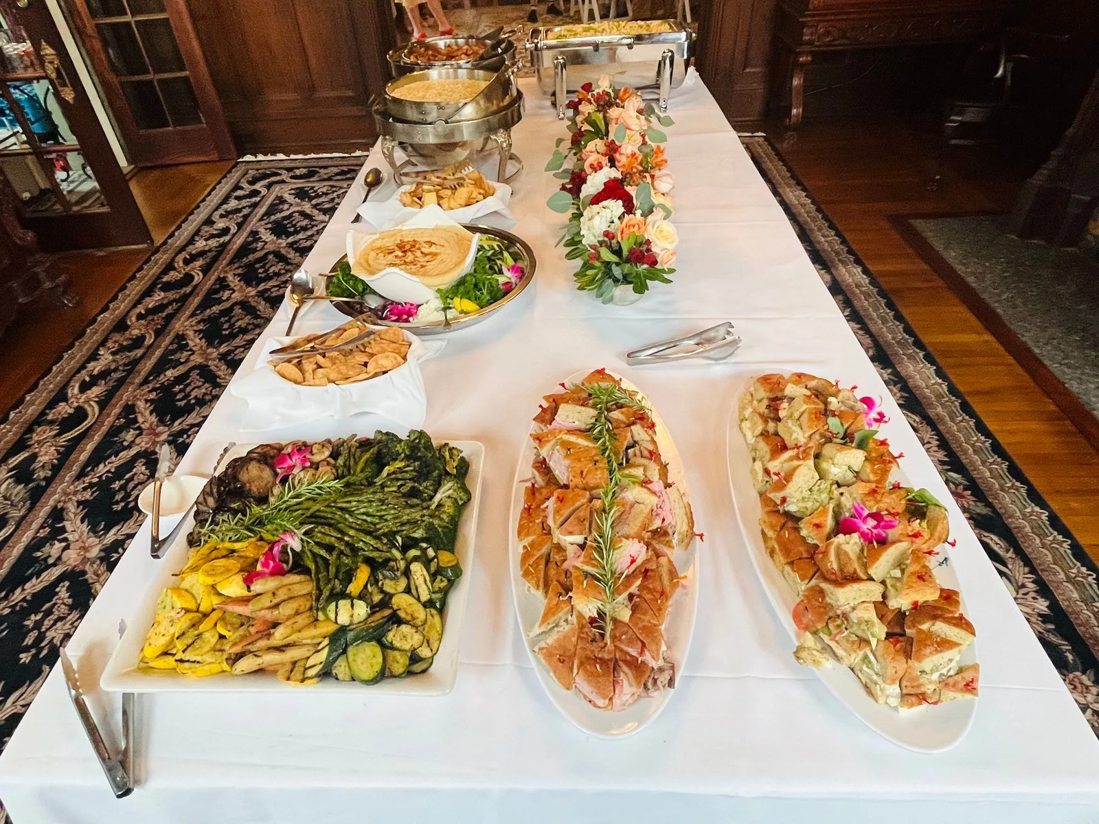 Buffet table with grilled vegetables, prosciutto-wrapped crostini, and fresh flower centerpiece