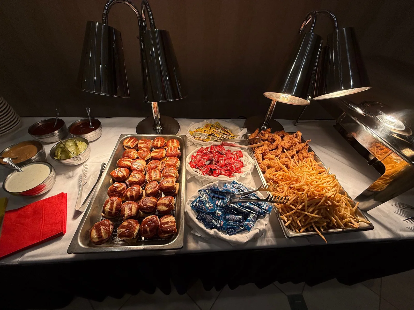 Hot buffet station with sliders, roasted peppers, fried shrimp, and french fries under heat lamps
