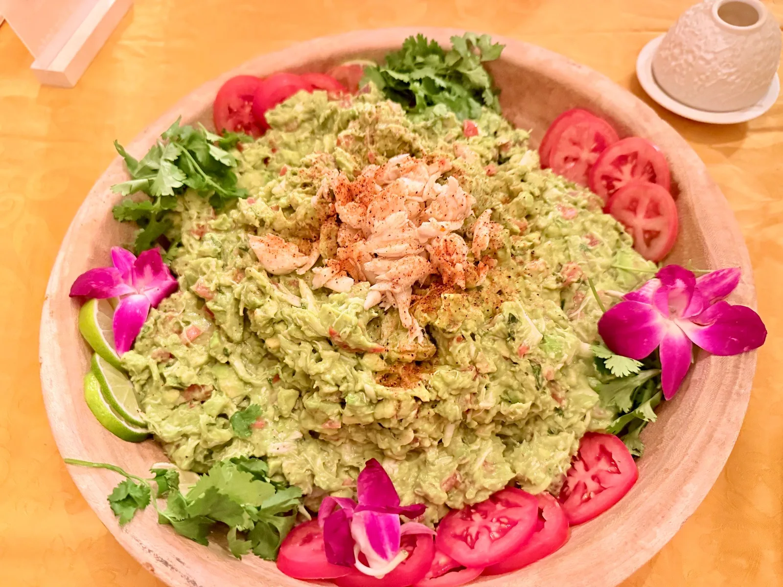 Guacamole topped with salmon, garnished with tomatoes, cilantro, and orchids