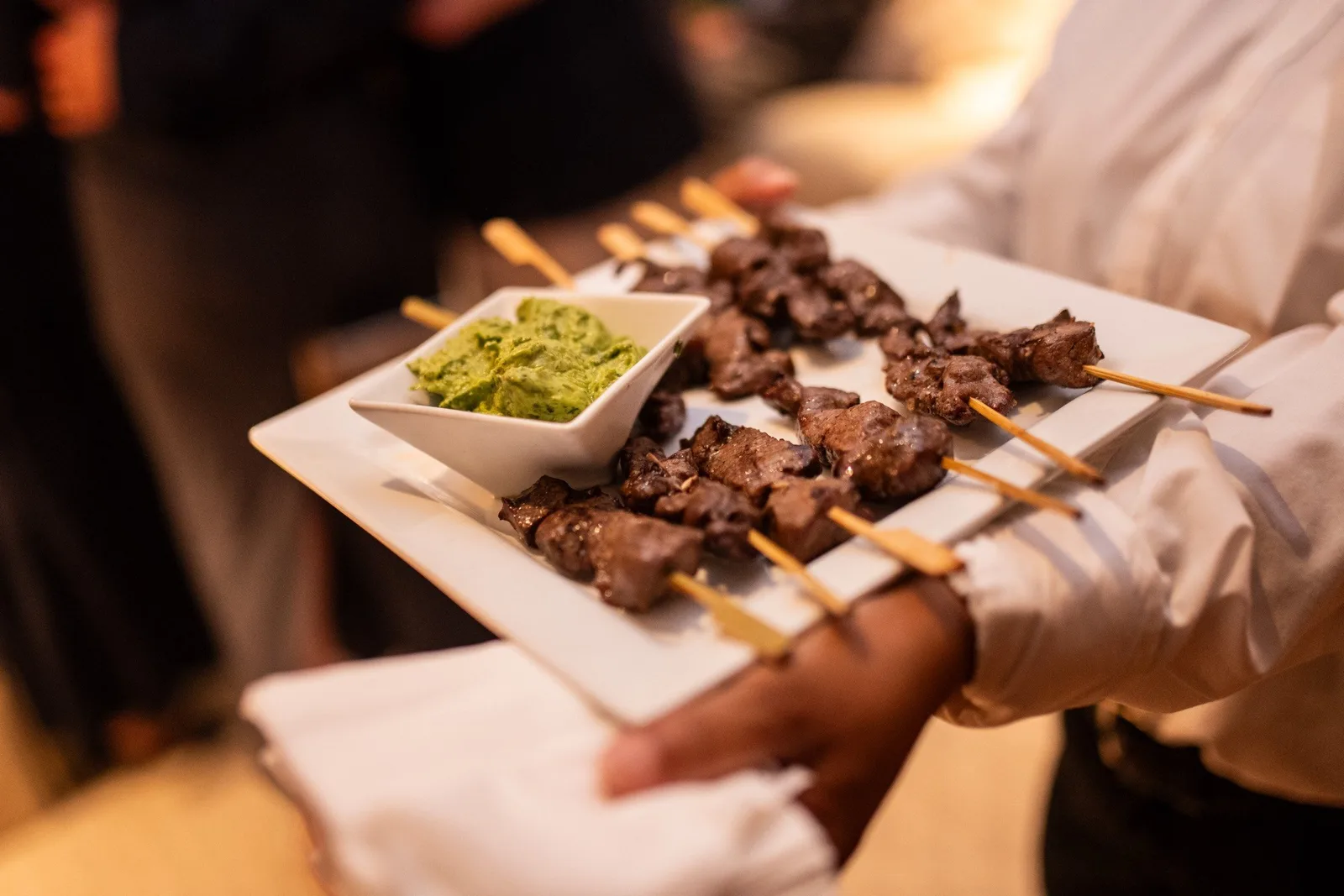 Server presenting beef skewers with chimichurri sauce at a catered event