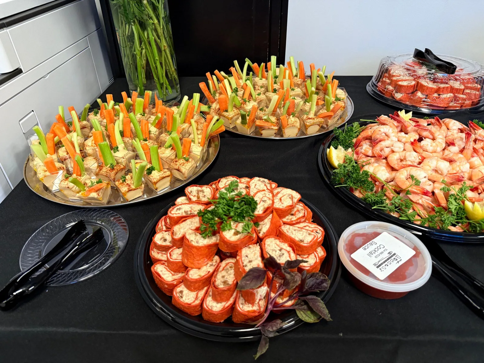 Appetizer spread with pinwheel sandwiches, crudité platters, boiled shrimp, and cocktail sauce