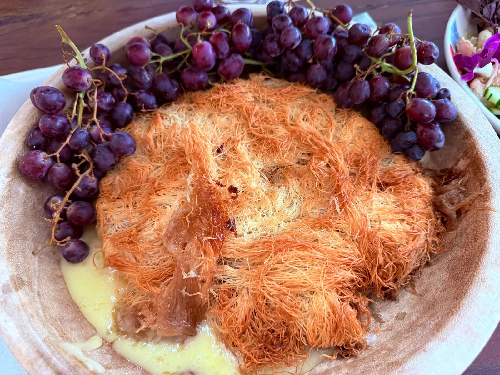 Baked brie wrapped in kataifi pastry with grapes on a wooden board
