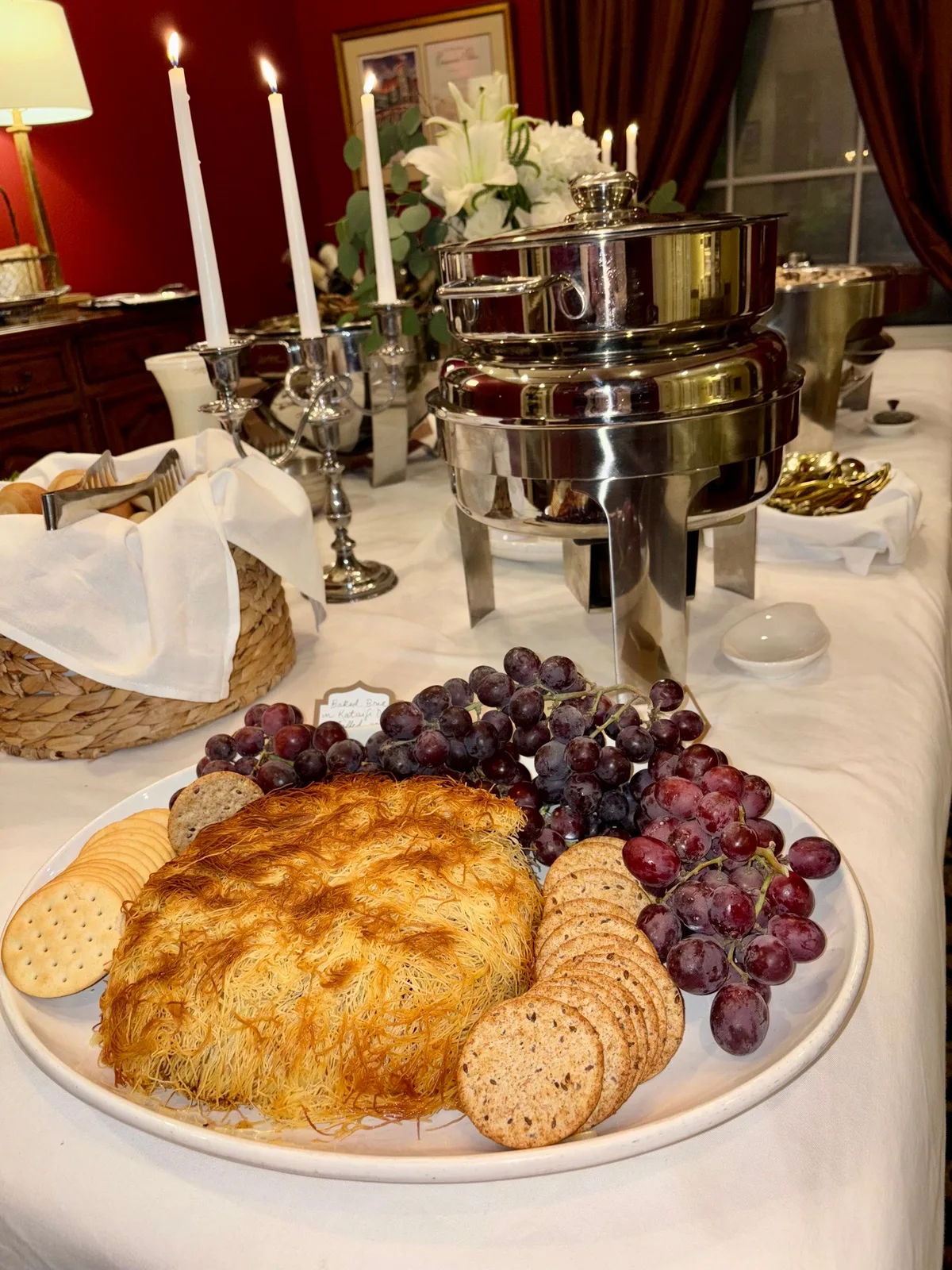 Baked brie with crackers, grapes, and chafing dishes on a candlelit buffet table
