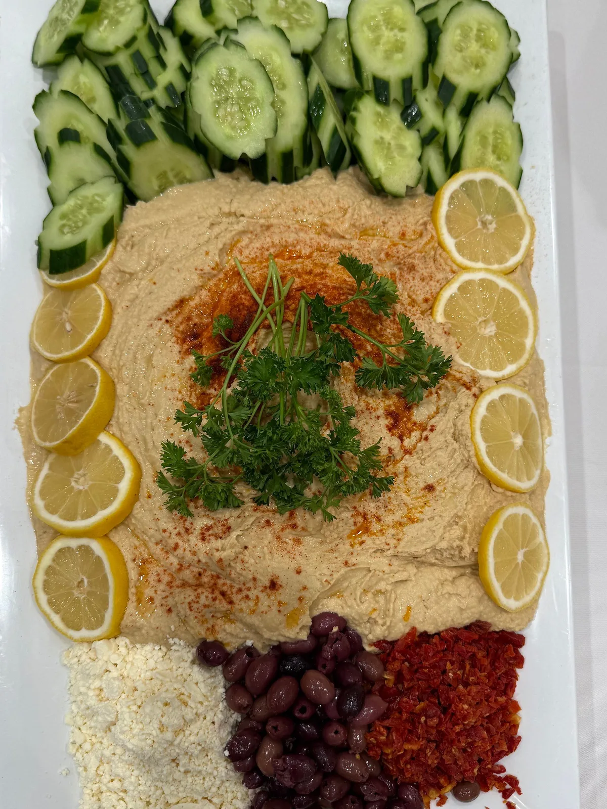 Hummus platter with sliced cucumbers, lemon wheels, olives, and sun-dried tomatoes