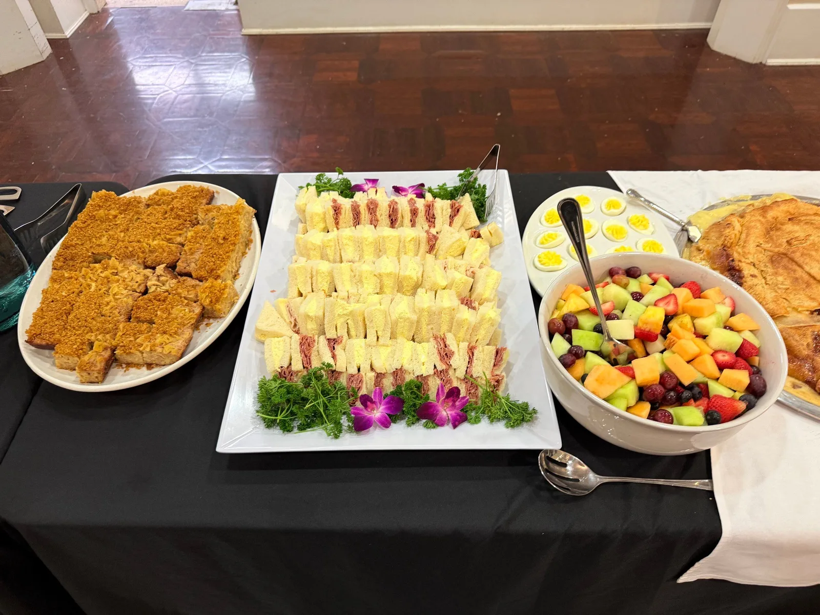 Brunch spread with fried chicken strips, finger sandwiches, fresh fruit bowl, and deviled eggs