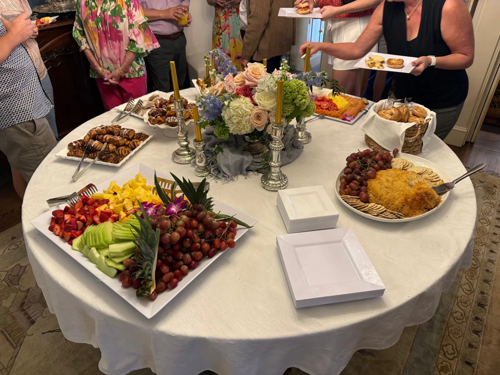 Round table event with fruit, bruschetta, cheese, and guests mingling