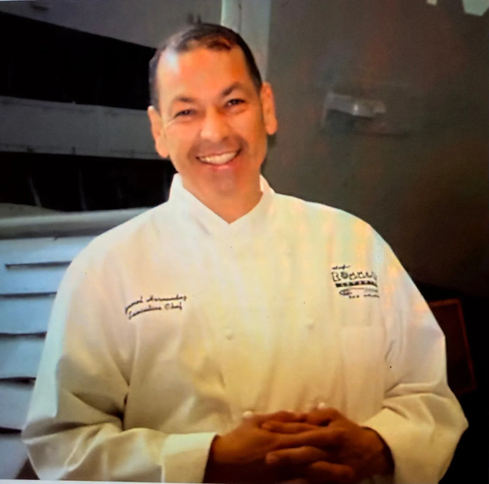 Chef Rommel Hernandez smiling in his white executive chef coat
